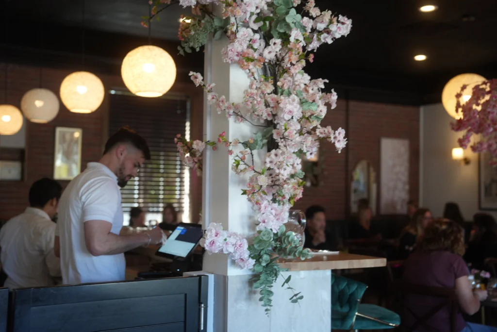 Morning Bloom team member at the counter beneath a blossom installation while guests dine