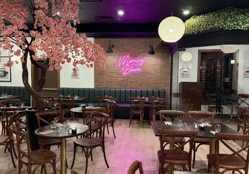Morning Bloom dining room with a pink blossom tree, a pink neon Morning Bloom sign on brick and green booth seating